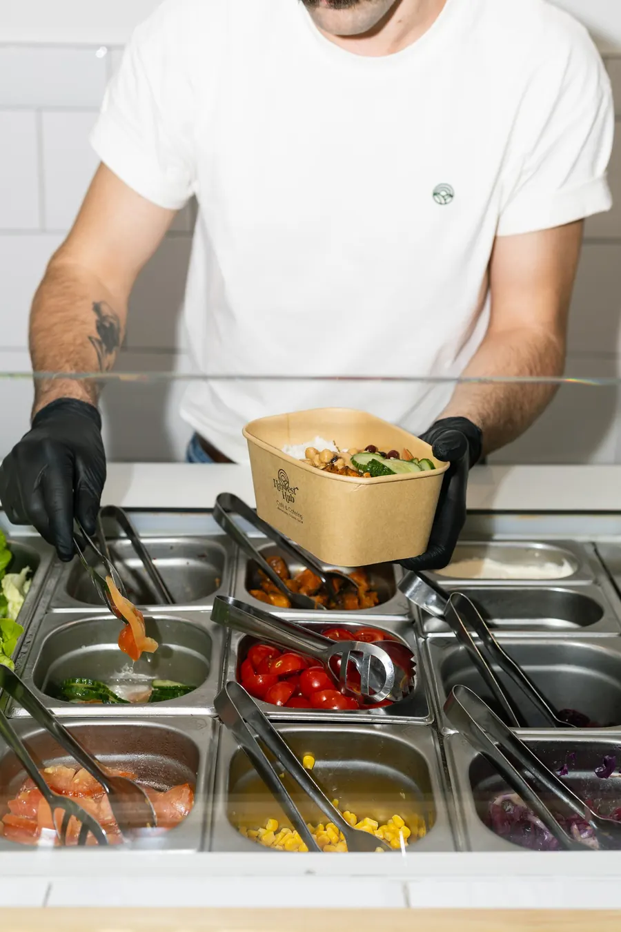 Een medewerker vult een bowl aan de toonbank met verse ingrediënten