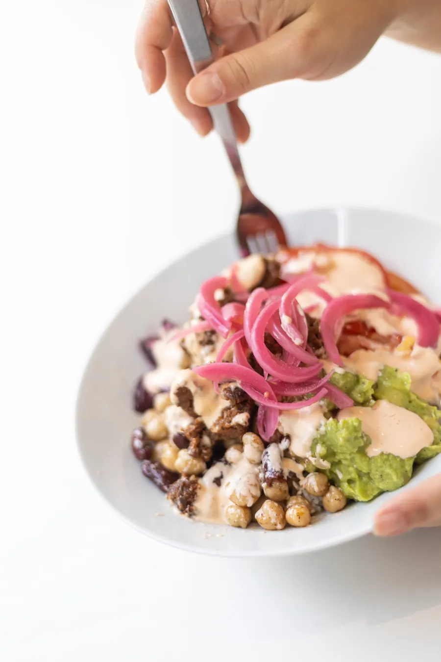 Een vork prikt in een bowl met kikkererwten, avocado en ingelegde rode ui
