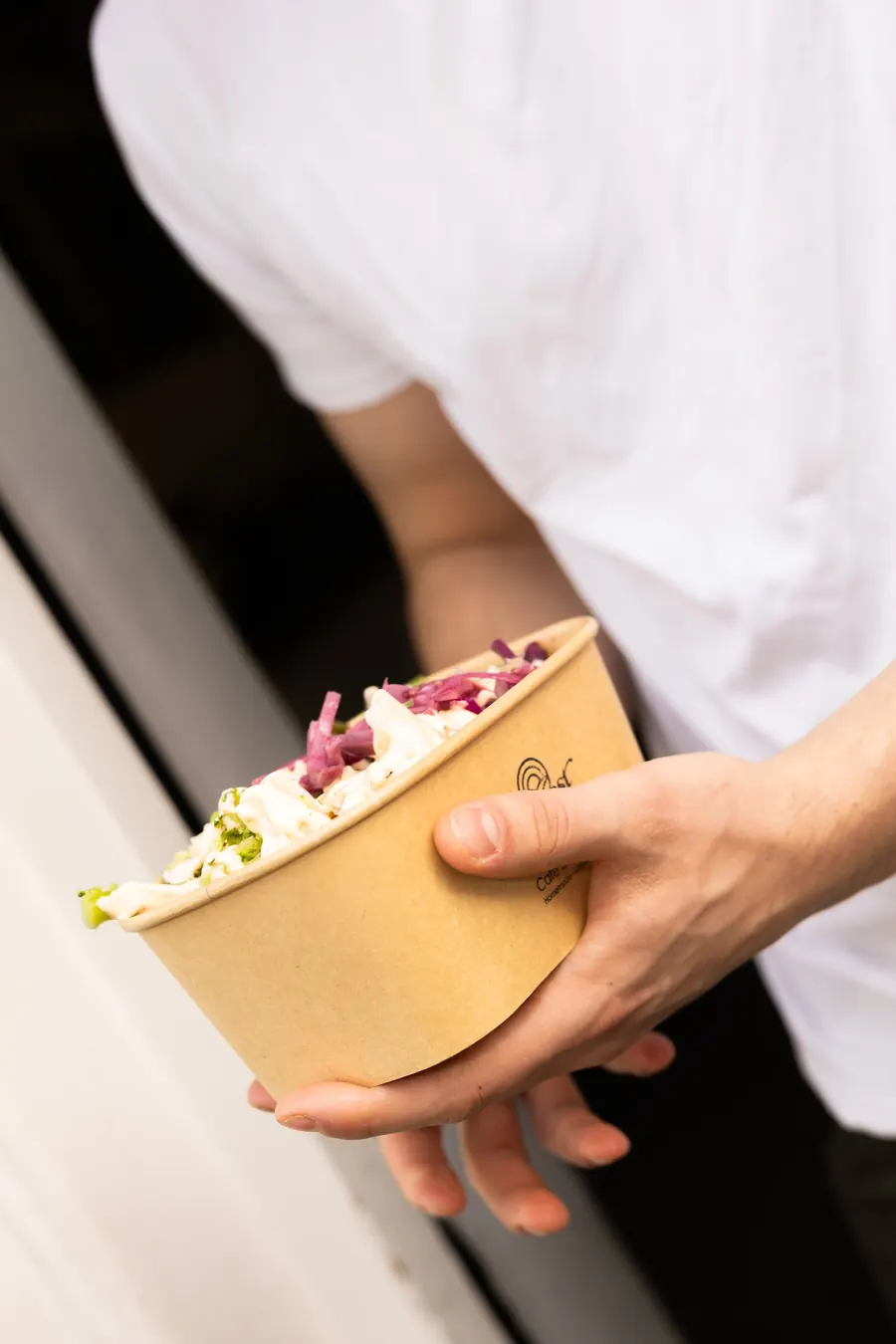 Een hand houdt een bowl in een kartonnen Harvest Hub-bak vast